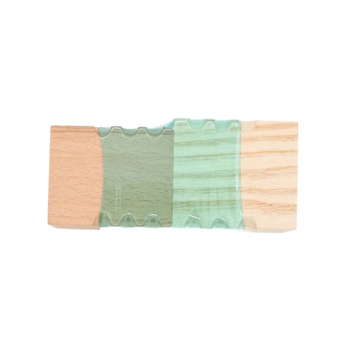 The block face-on, the mint-green plastic band gripping pale wood on each side with its scalloped edges interlocking.