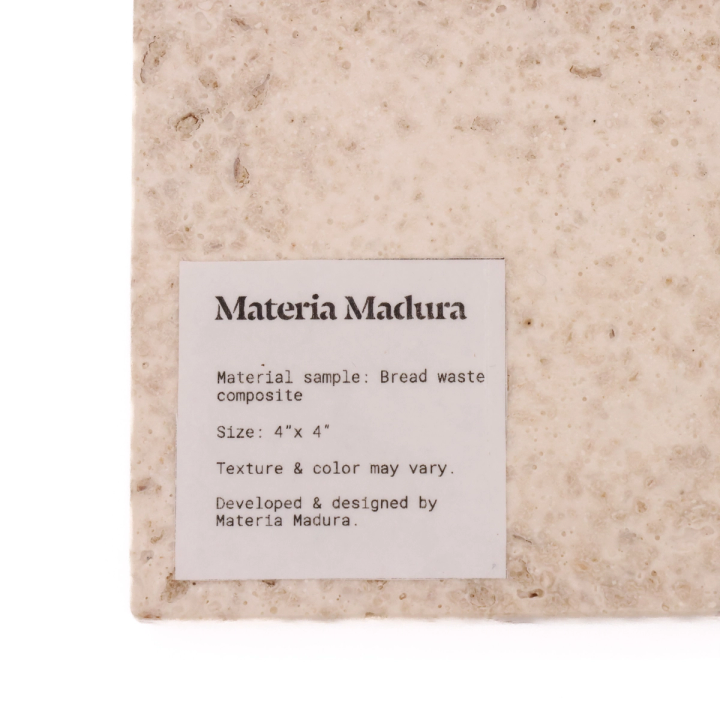 The tile face-on with a printed label reading “Materia Madura — Material sample: Bread waste composite, Size 4″ x 4″. Texture & color may vary.”