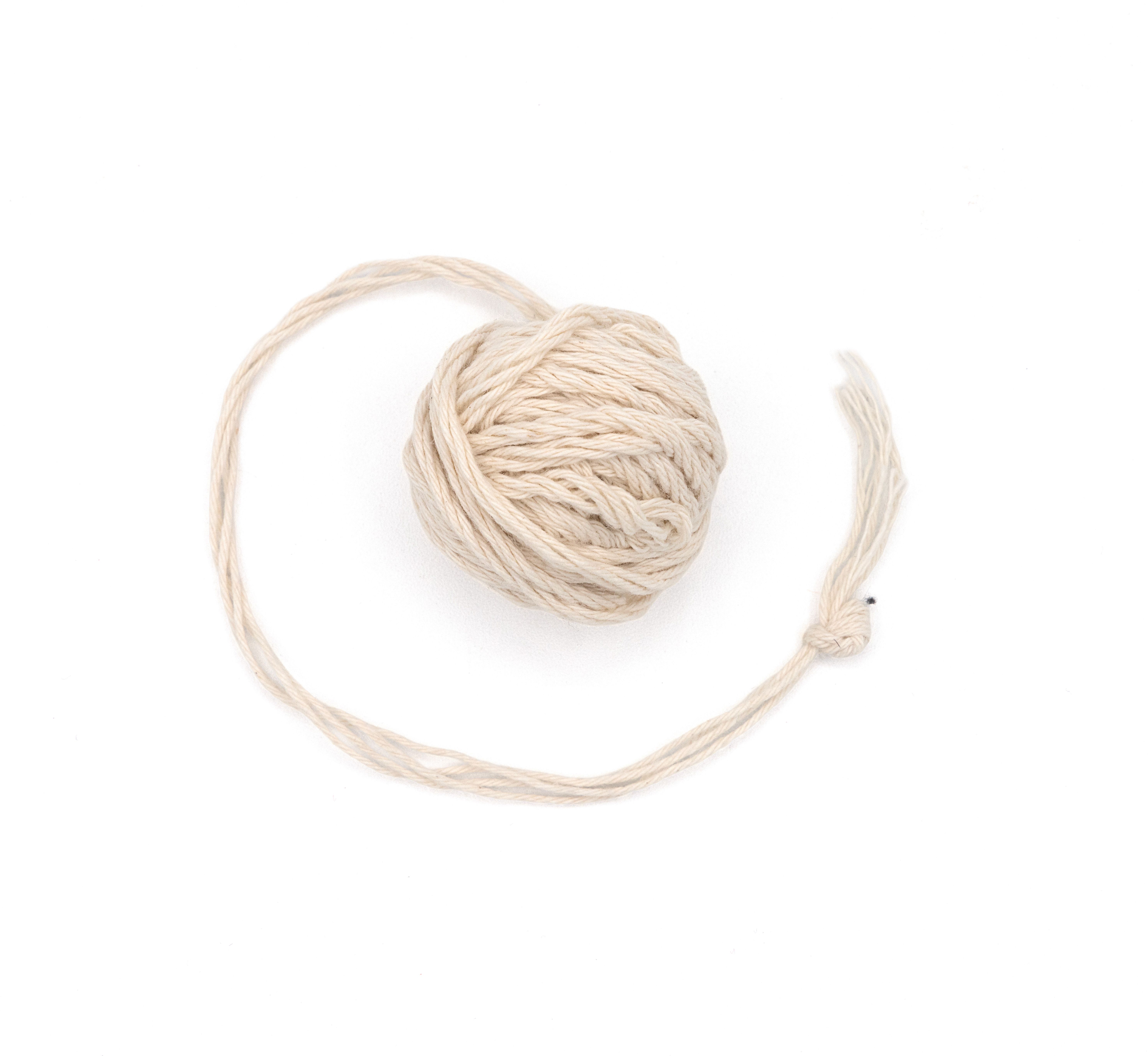 A small ball of undyed cream cotton yarn, a long loose strand curving out and looping around it.