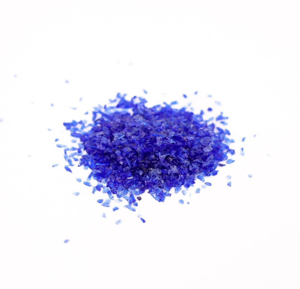 A loose mound of coarsely crushed glass in vivid cobalt, the angular chips catching the light, with stray fragments scattered around the base.