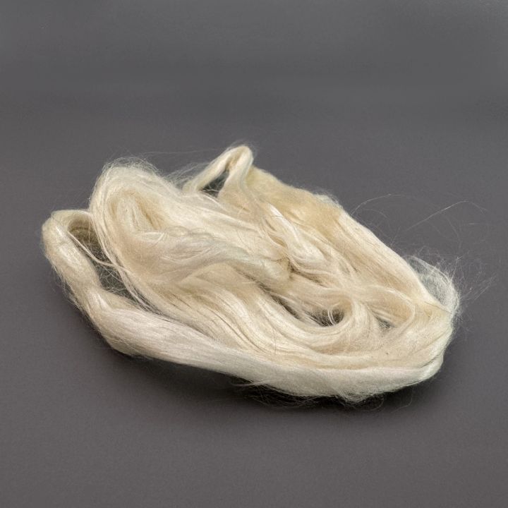 The same silk seen closer and against a dark ground, the long filaments smooth and lustrous with the loops splayed open.