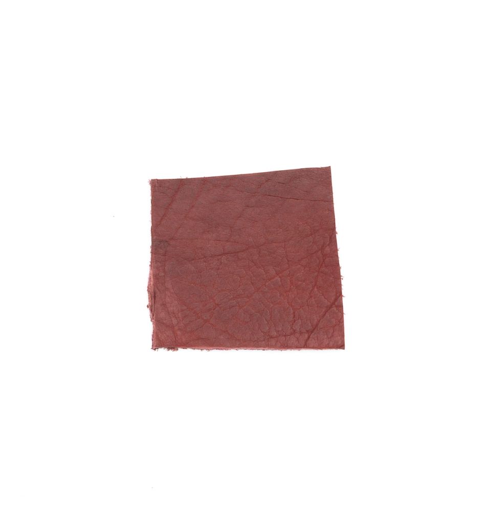 A square of vegetable-tanned cowhide in deep oxblood red, its surface faintly veined with a natural grain.
