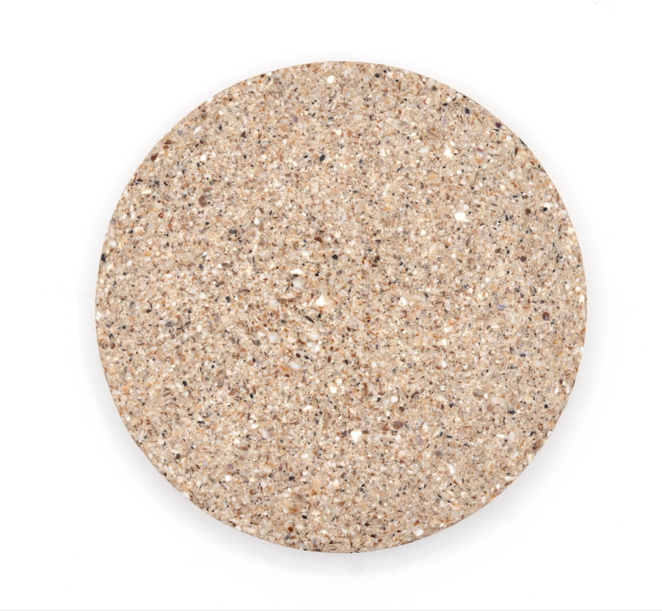 A larger round tile of dense composite in pale oatmeal, evenly speckled with fine crushed shell.