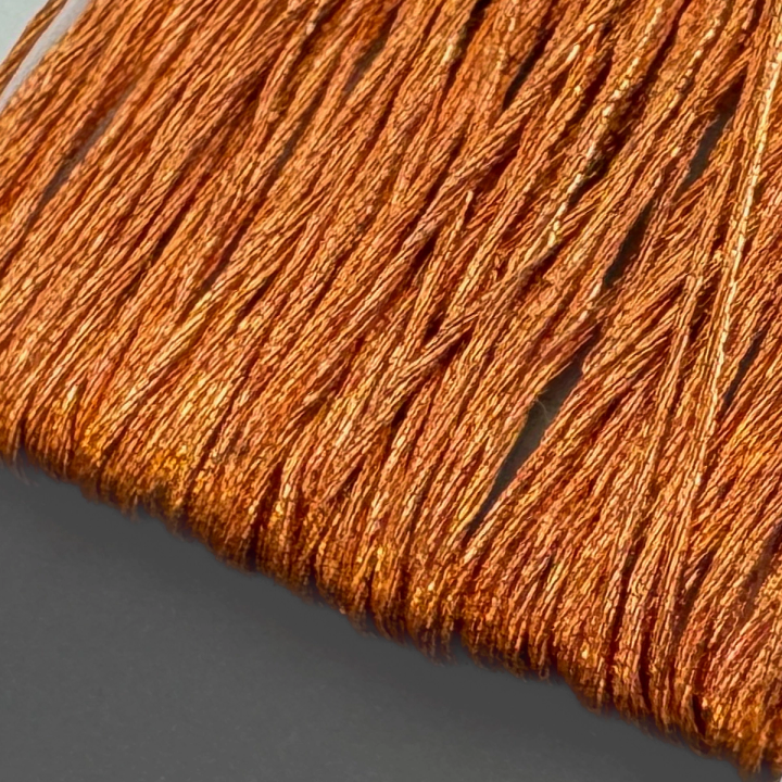 A close view of the wound thread, its metallic copper strands catching the light in bright bands and lying in tight parallel rows.
