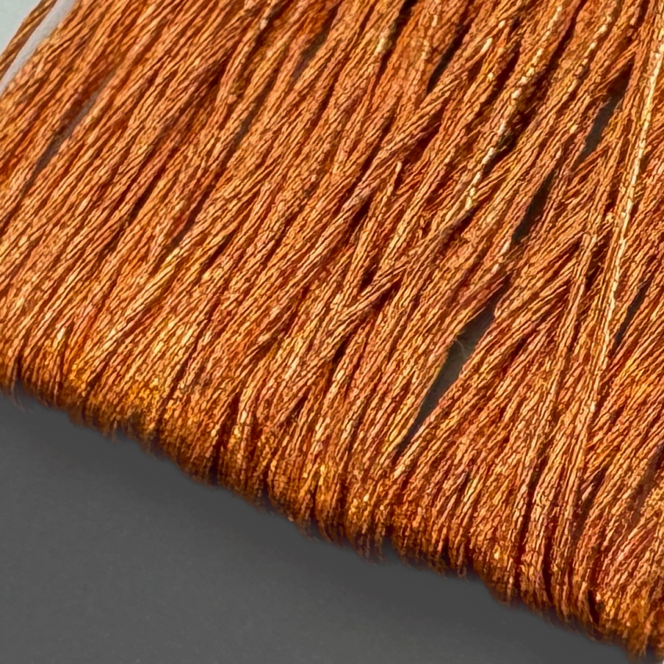 A close view of the wound thread, its metallic copper strands catching the light in bright bands and lying in tight parallel rows.