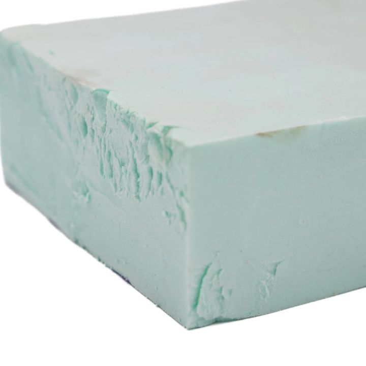 A thick block of pale mint foam seen close at the corner, its cut faces smooth but torn and crumbling along one edge.