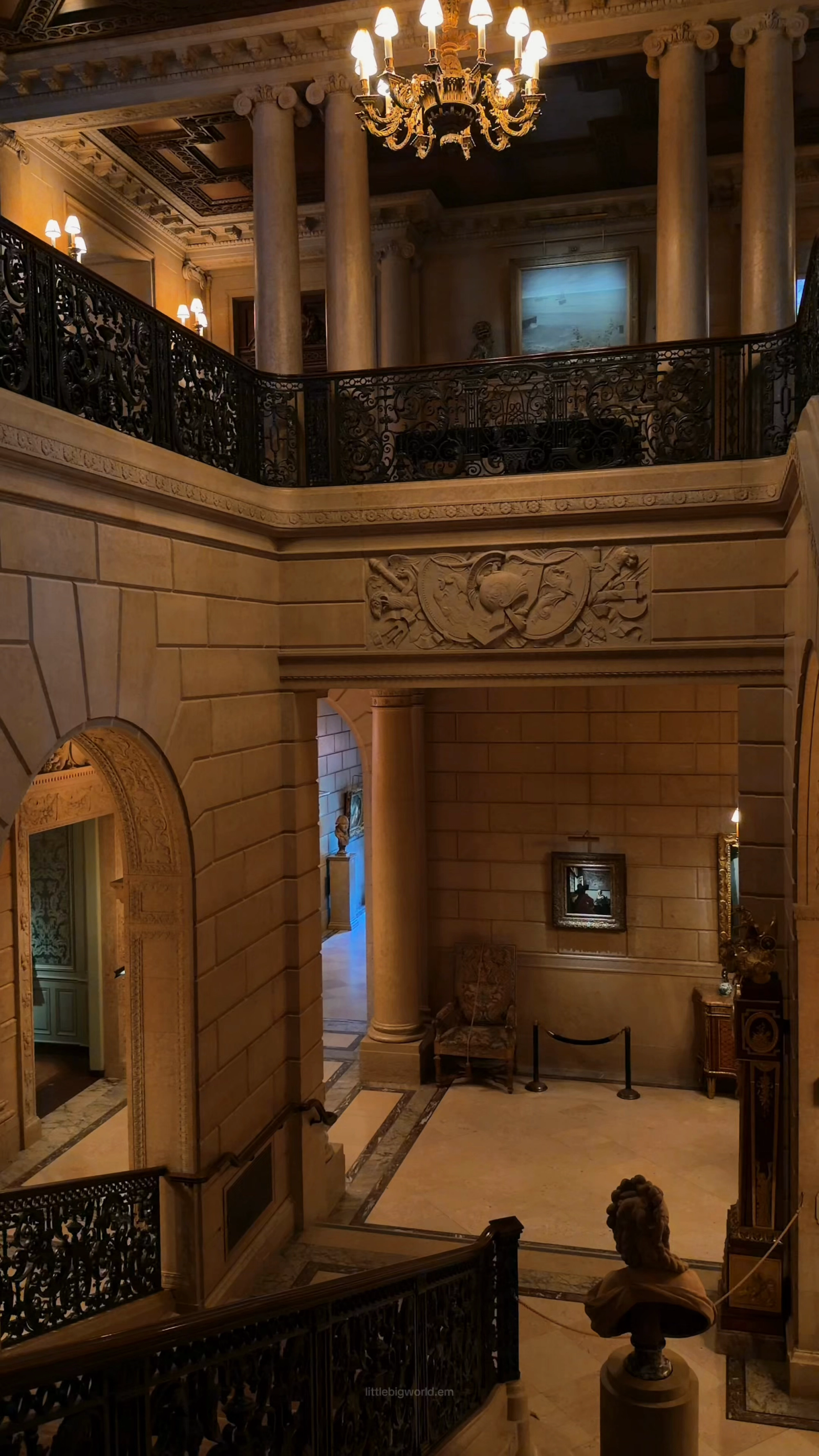 An ornate stair hall with carved stone, gilding, and dark balustrades at the Frick.