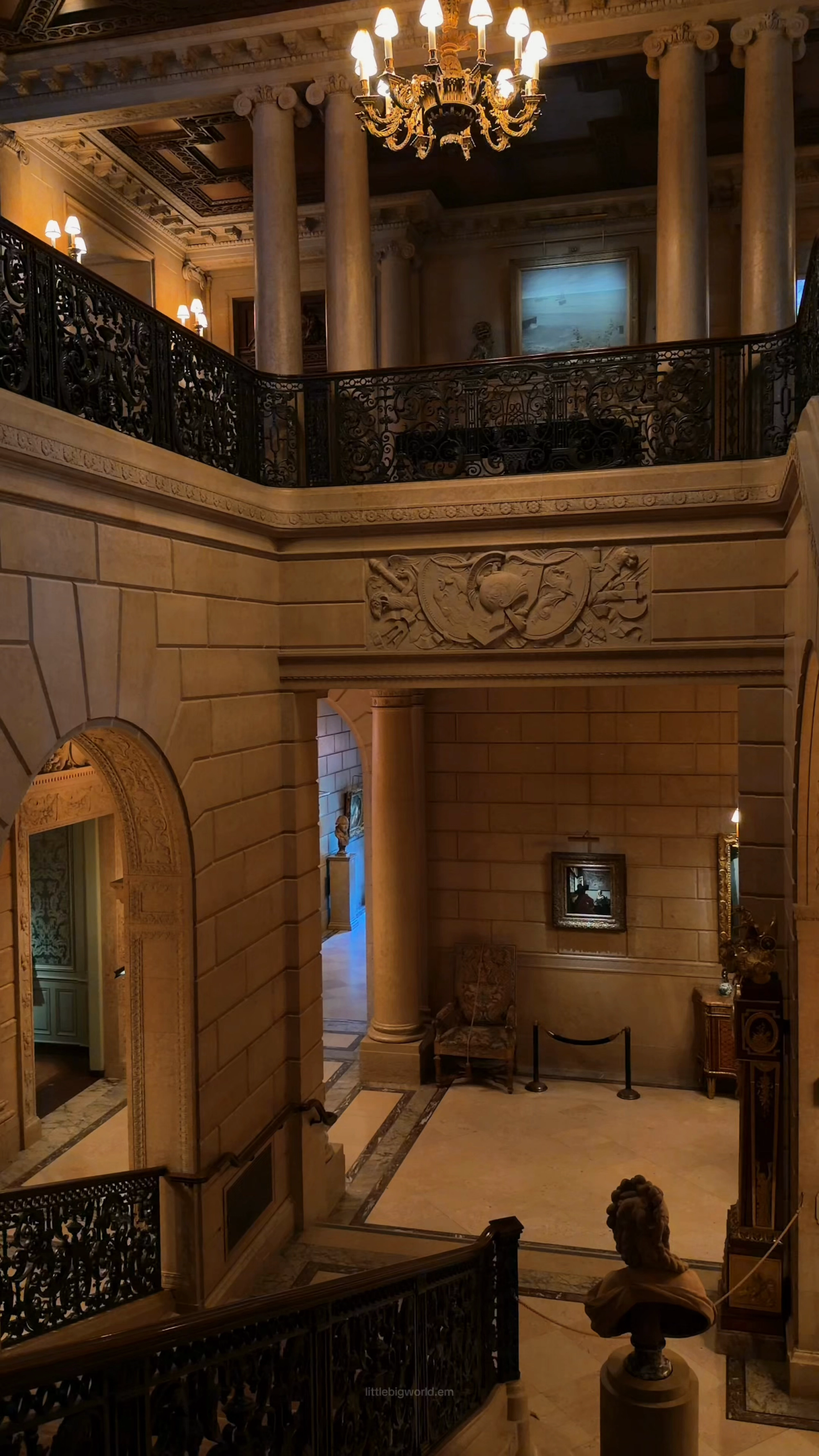 An ornate stair hall with carved stone, gilding, and dark balustrades at the Frick.