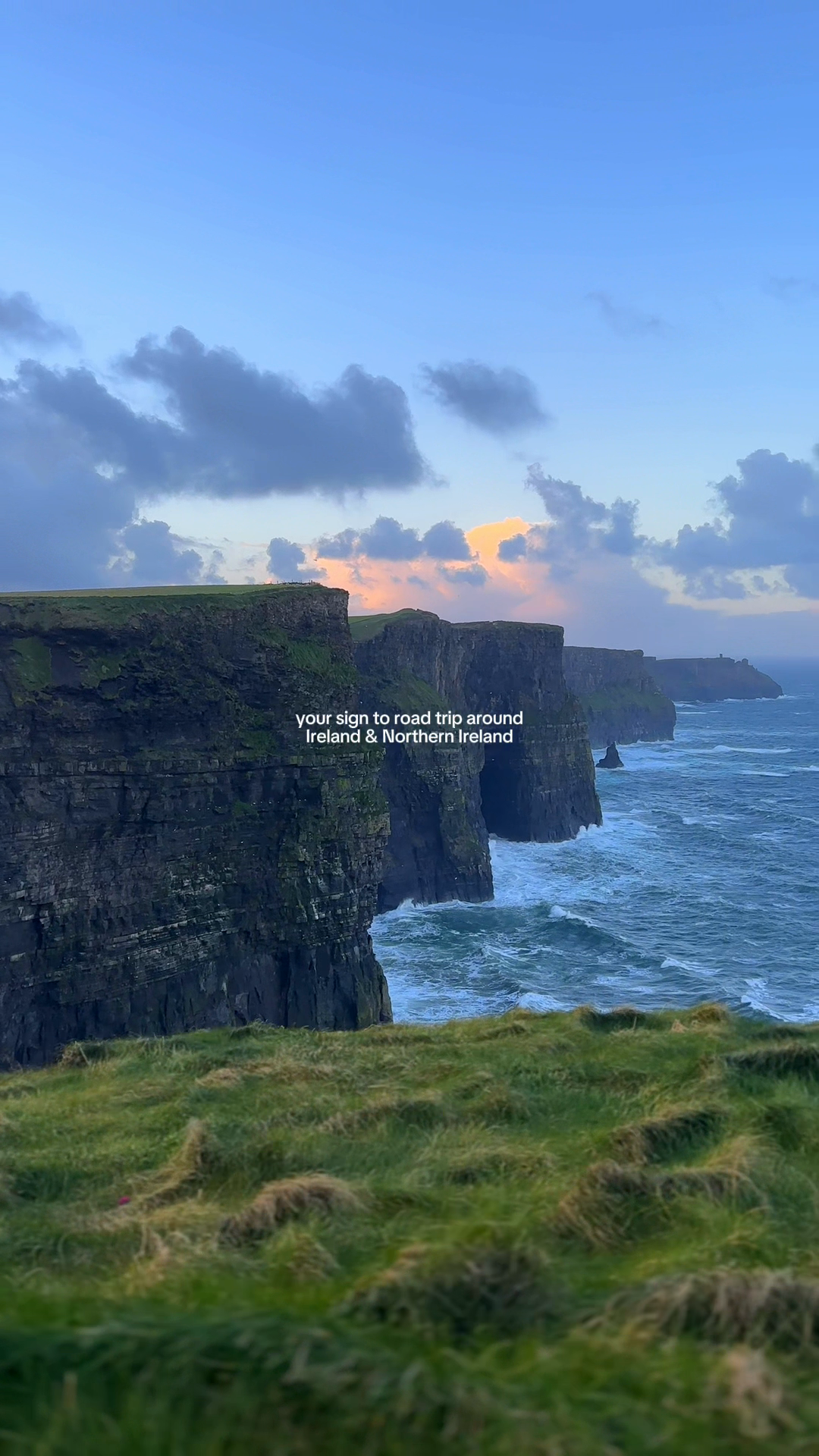 Green sea cliffs above a dark Atlantic shoreline at dusk.
