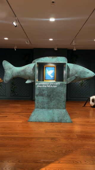 A green fish sculpture surrounds a framed bird painting.