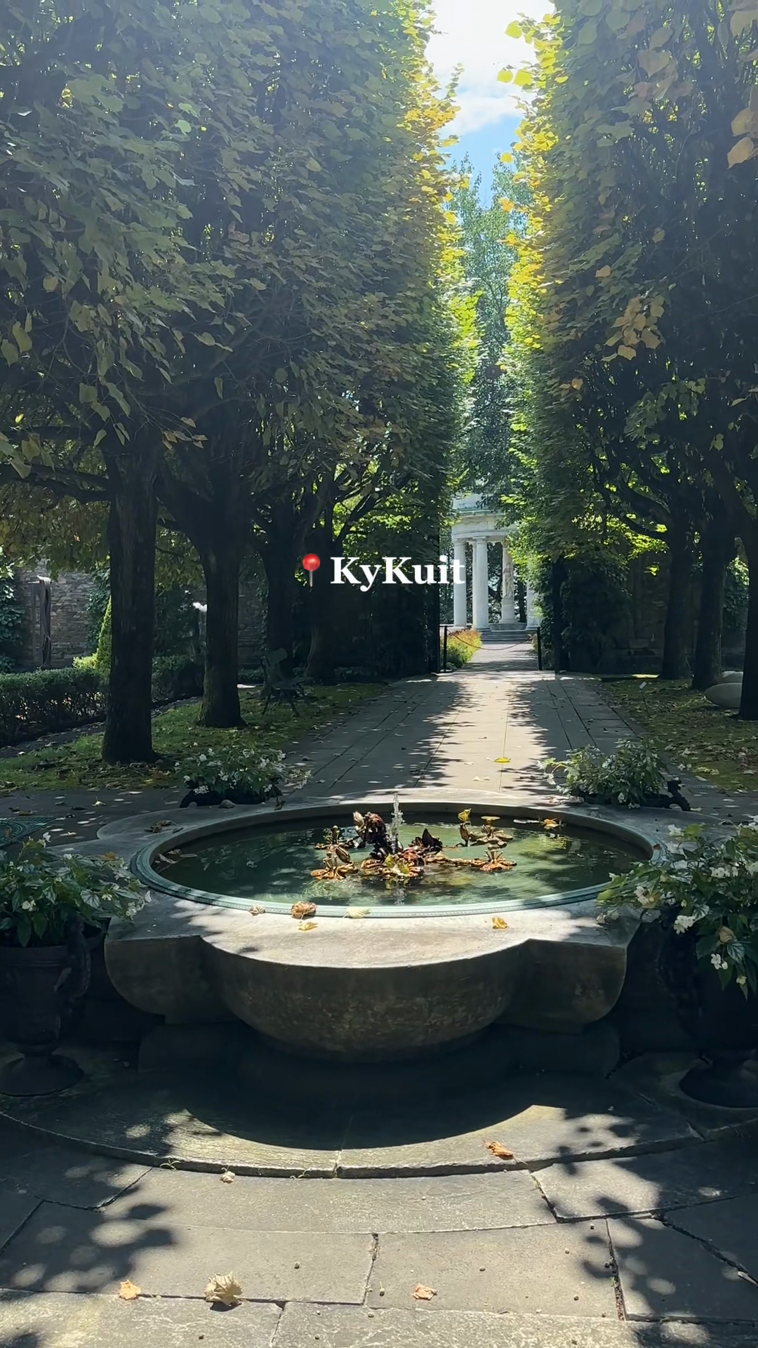 A round fountain at the end of a tree-lined garden walk.
