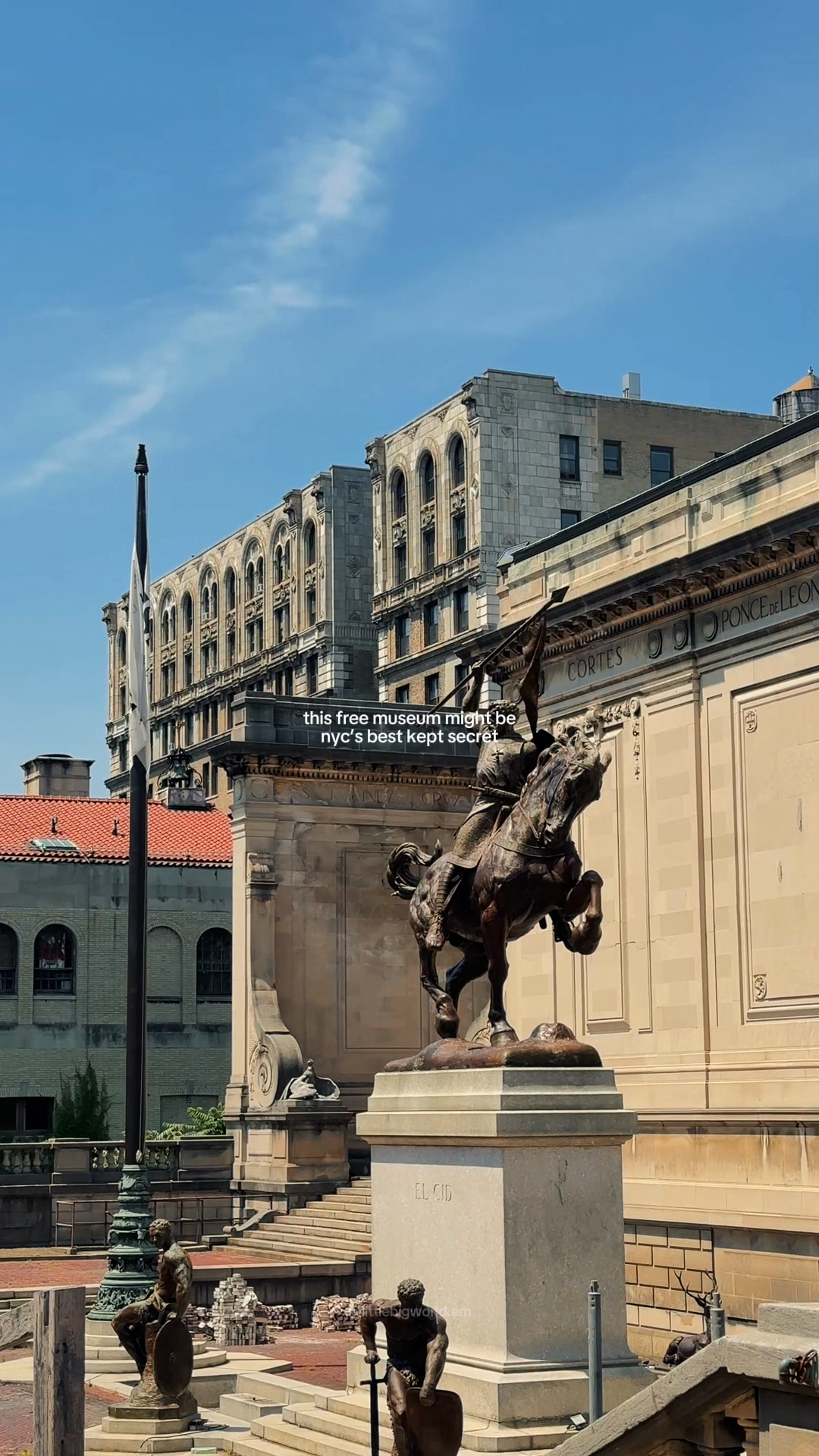 An equestrian bronze statue and museum facade in a sunlit terrace.
