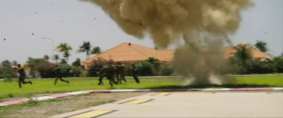 An explosion on a lawn between palm trees, soldiers running.