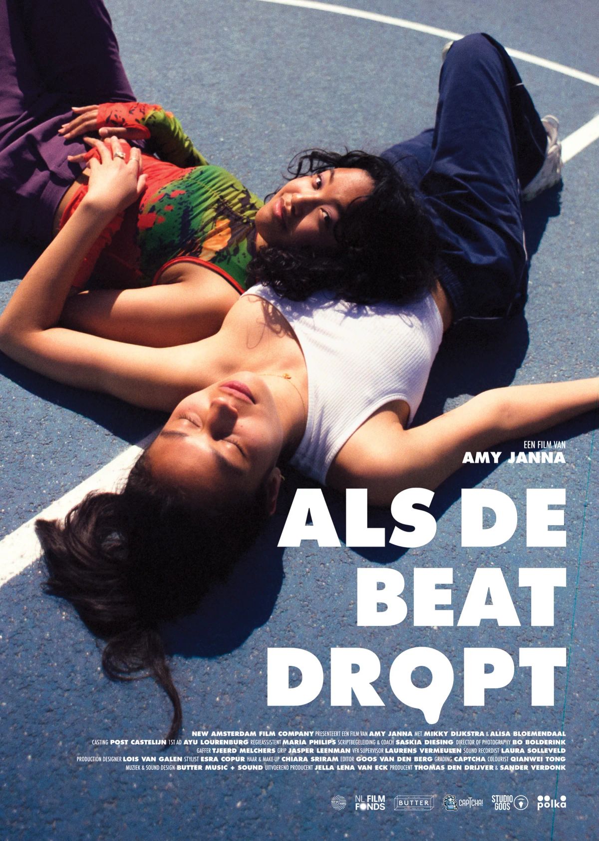 Poster: two girls lie with their eyes closed on the blue tarmac of a sports field.