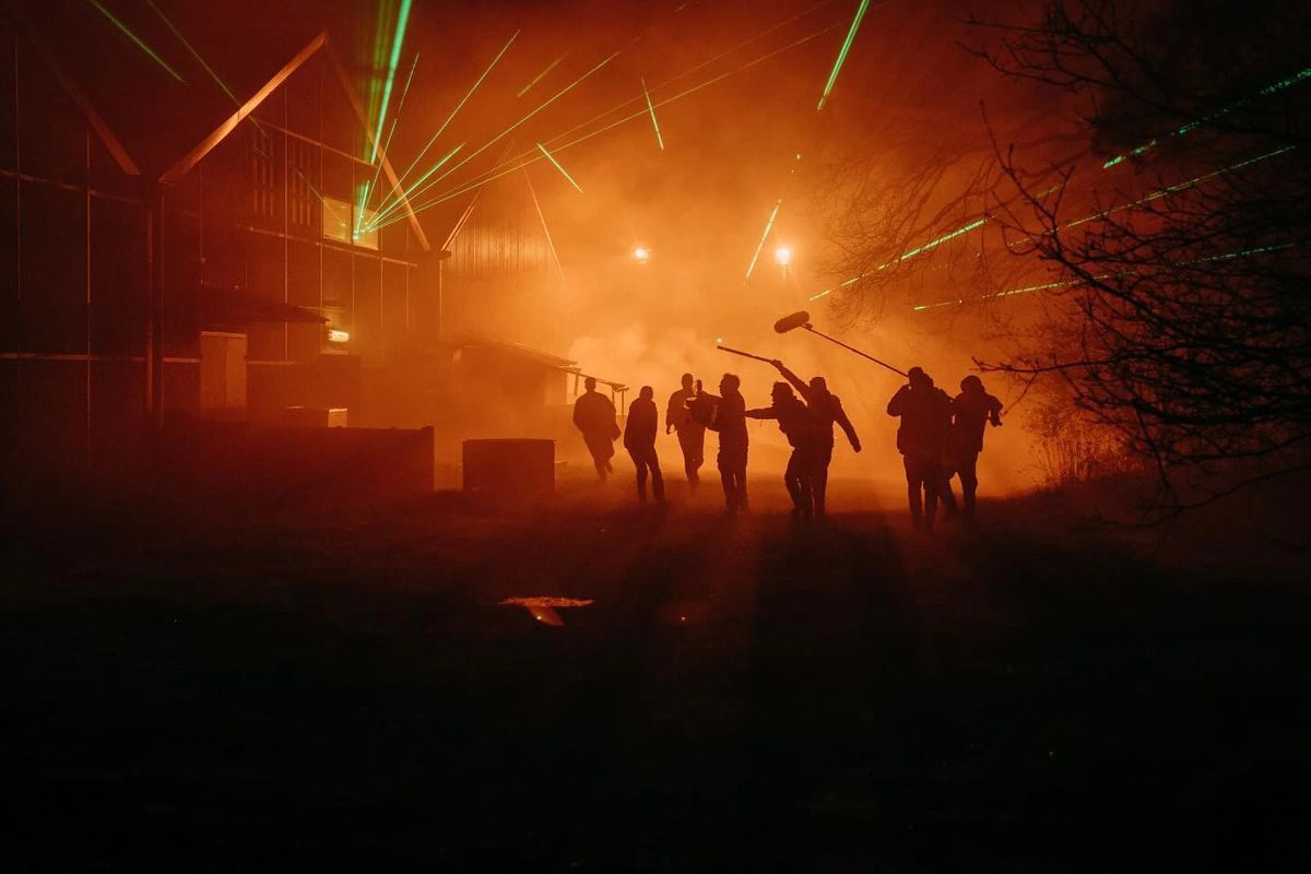 Silhouettes of crew with a boom microphone in orange haze.