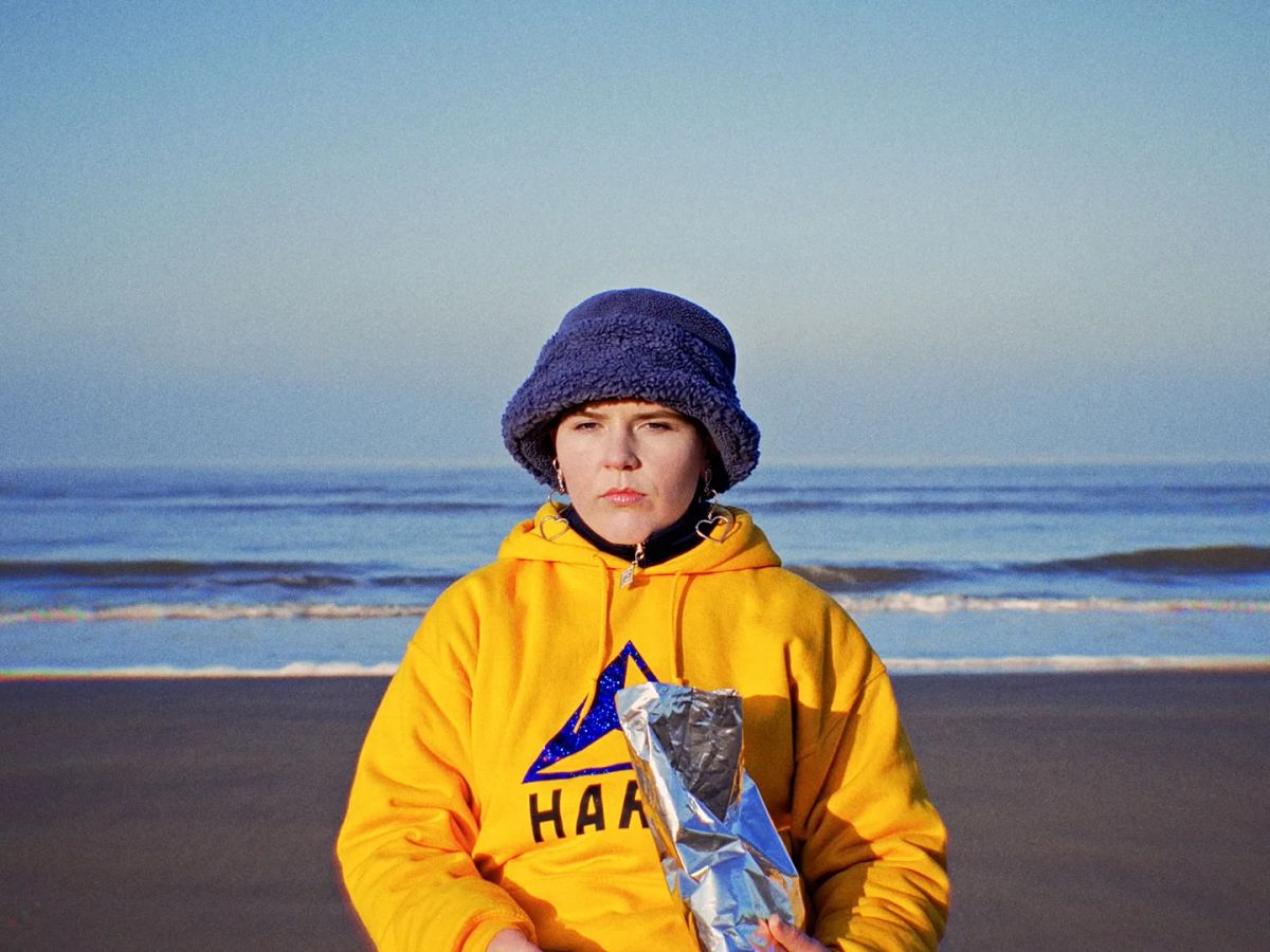 Someone in a yellow hoodie and a purple bucket hat on the beach at dusk.