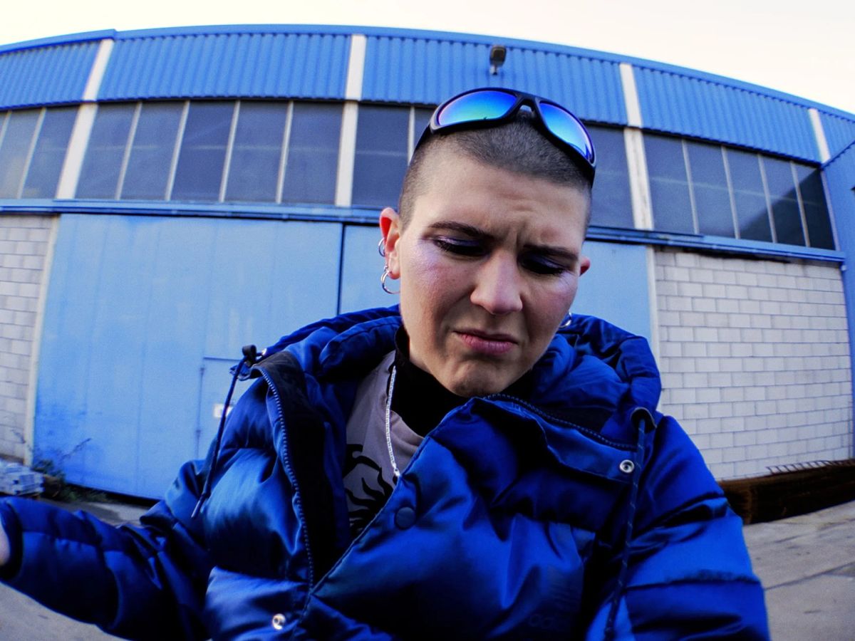Fisheye: the artist in a blue puffer jacket in front of a blue hangar.