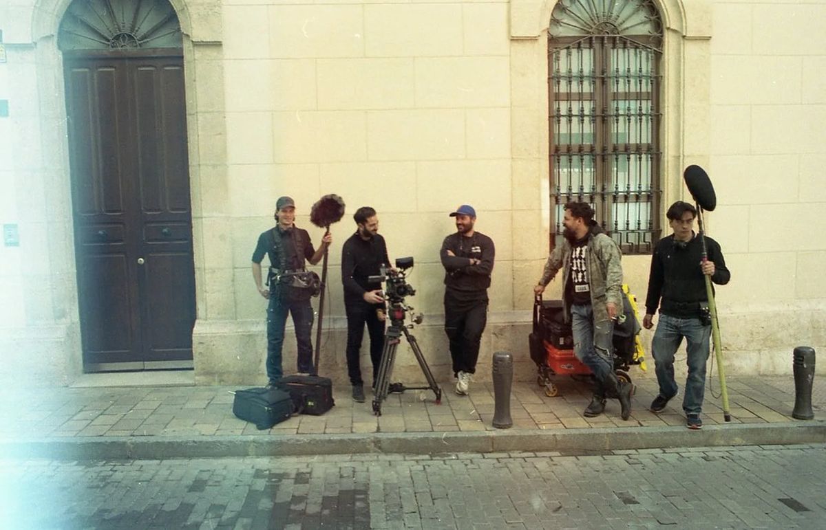 Analogue photo: crew with a boom microphone in a street in front of a yellow facade.