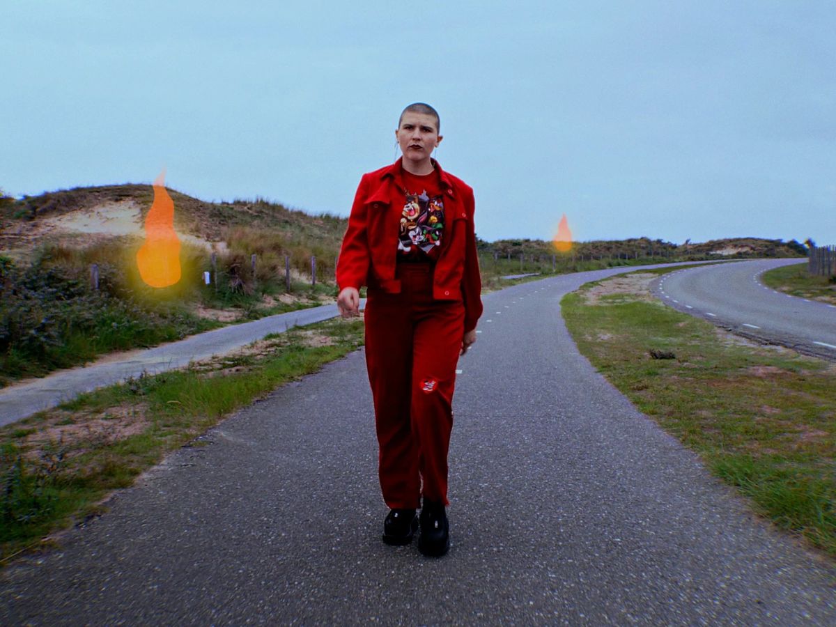 The artist in a red suit walks along a cycle path through the dunes, with drawn flames in the grass.