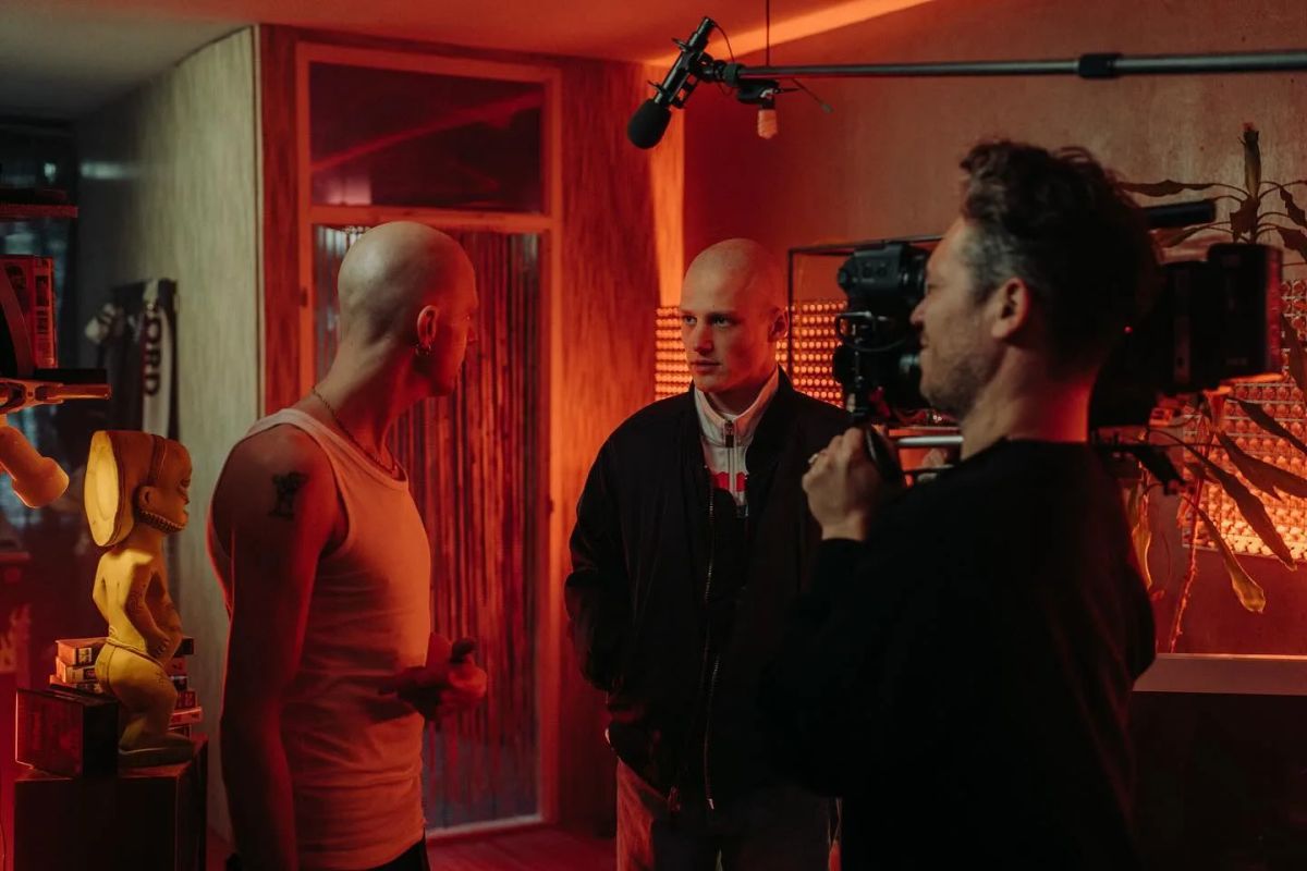 A camera operator and a boom in a red room, two actors in front of the lens.