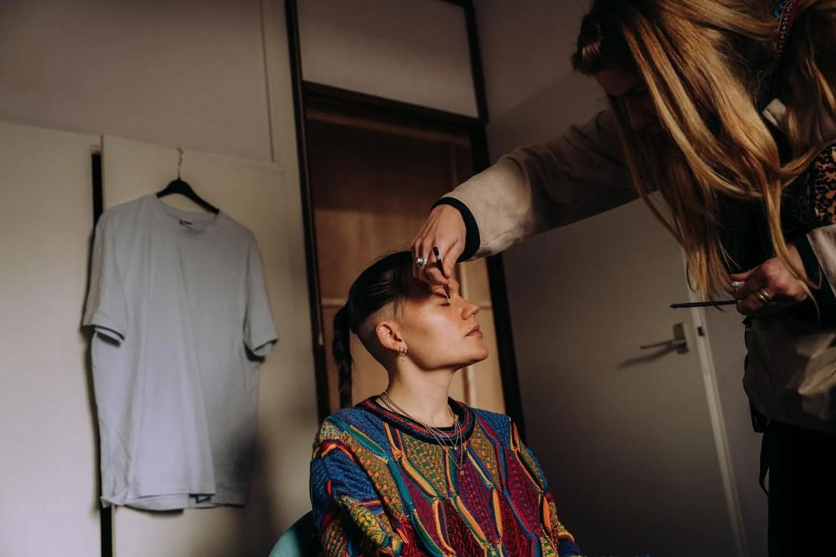 A make-up artist works on an actor in a colourful jumper.