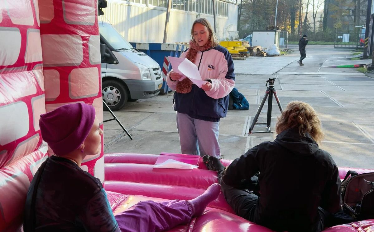 Behind the scenes of de laatste tijd: Amy with papers in her hand by a pink bouncy castle, crew around her.
