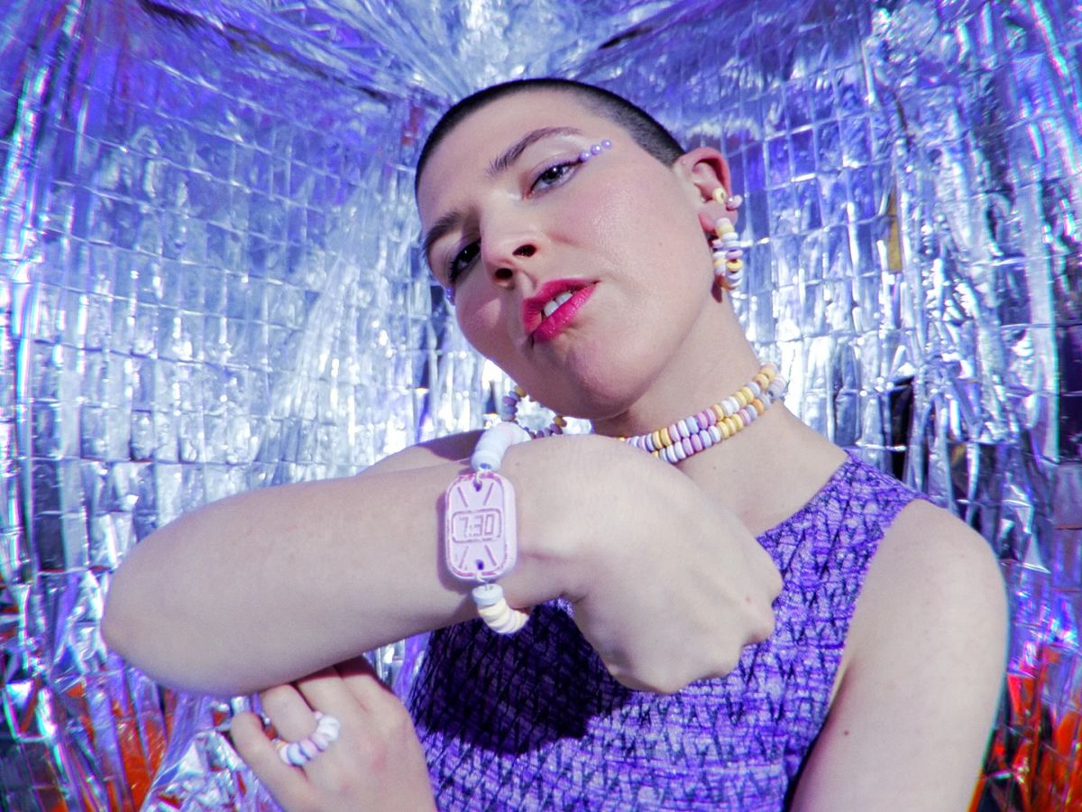 The artist in a room of silver foil, in a purple top and beaded bracelets, looks into the lens.