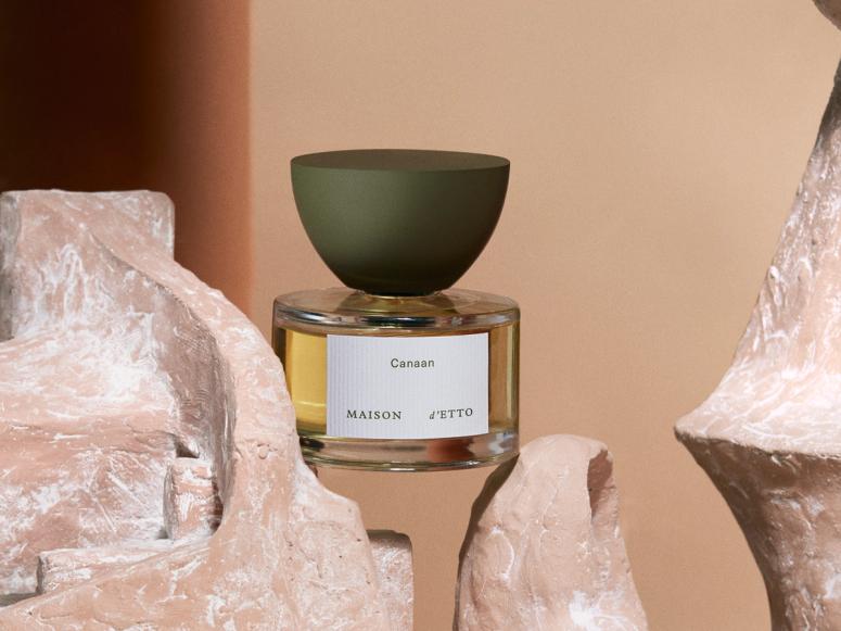 A sculptural bottle of perfume is balancing between two pieces of carved stone.