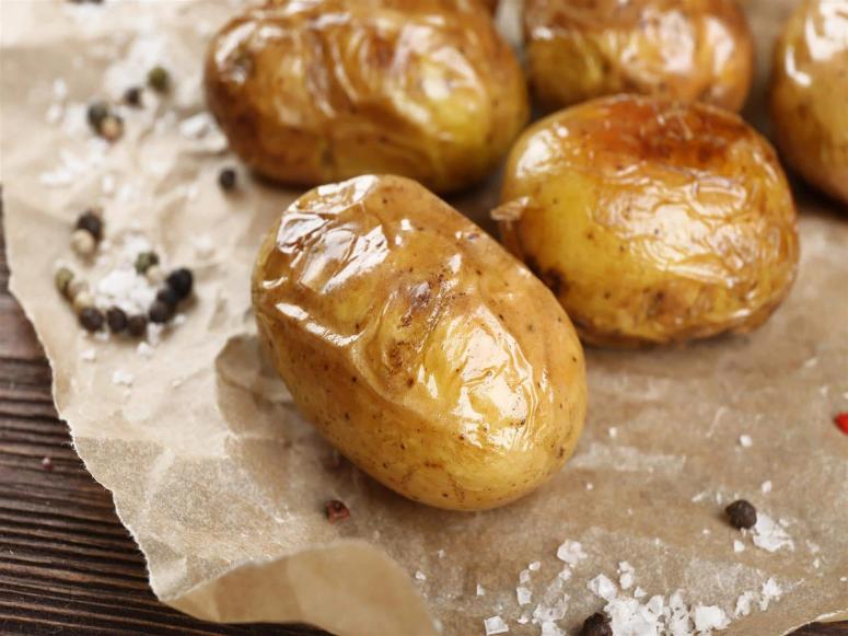 Baked potatoes sitting on wax paper with salt and pepper.