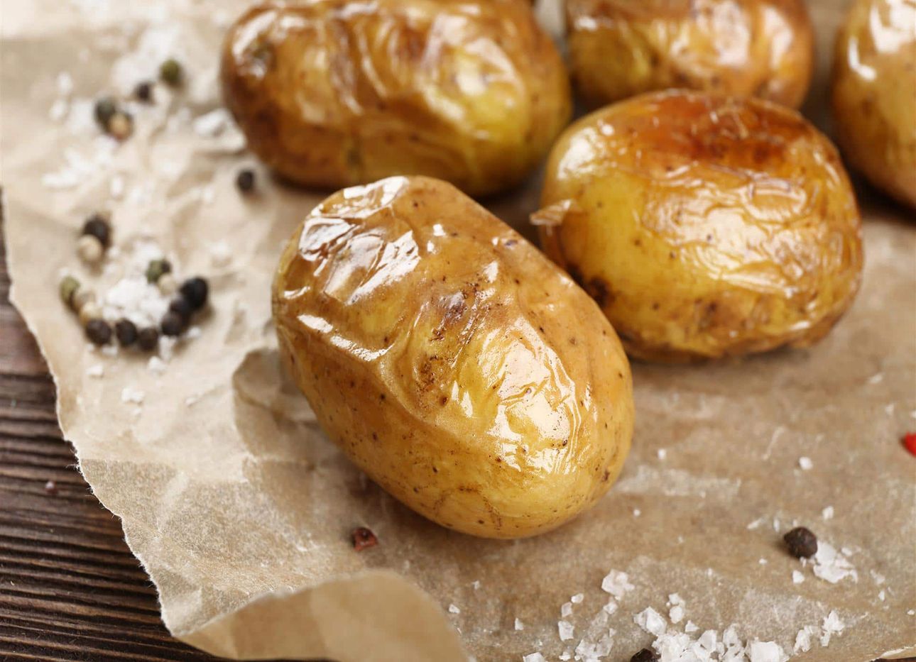Baked potatoes sitting on wax paper with salt and pepper.
