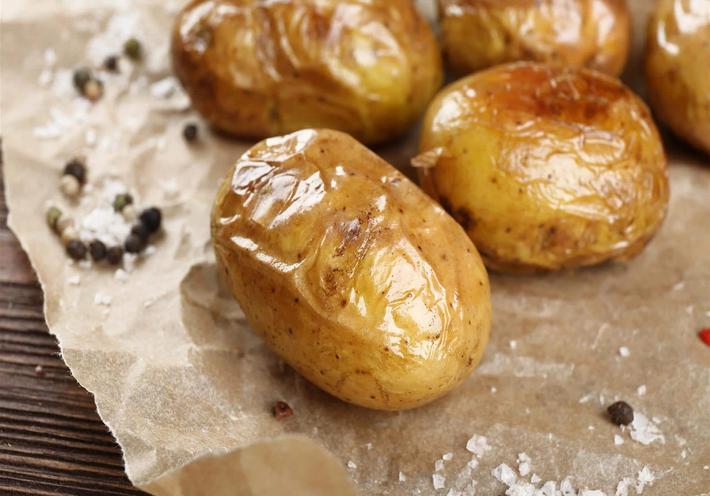 Baked potatoes sitting on wax paper with salt and pepper.