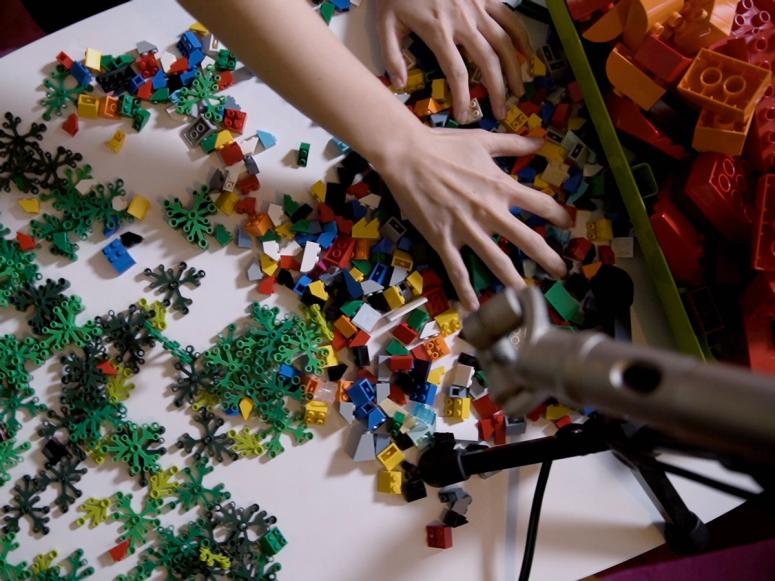 Two hands mixing up Lego pieces on a white table.