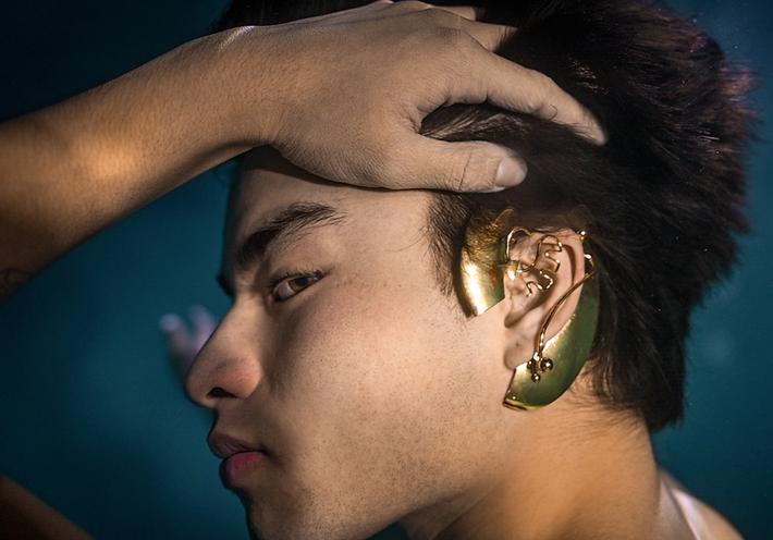 A man wearing gold ear jewelry underwater.