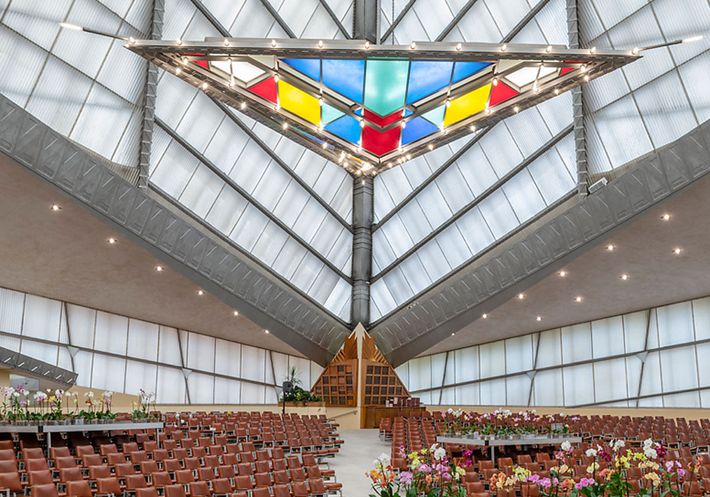 A large, open synagogue interior with a stained glass triangular chandelier.