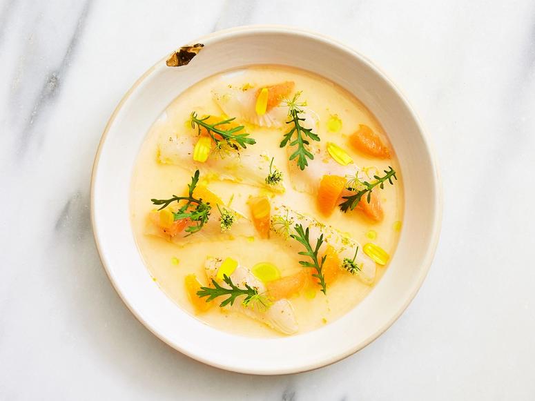 A bright white and orange bowl of soup on a marble surface.