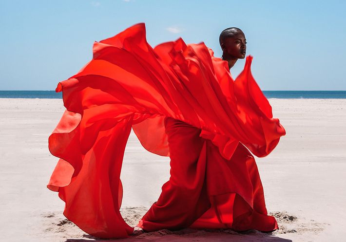 A photograph of a woman in a bright red dress on the beach.