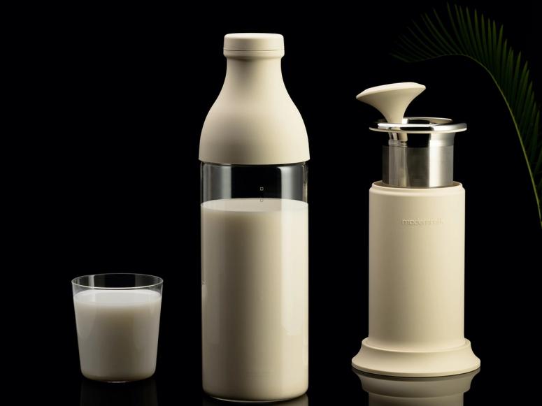 A white Modern Milk milk press and glass of milk on a black background.