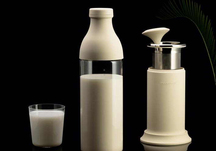 A white Modern Milk milk press and glass of milk on a black background.