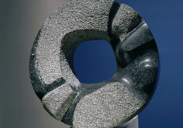 A doughnut-shaped stone Noguchi sculpture on a plinth.