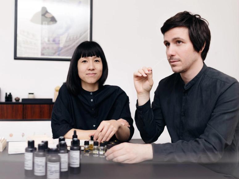 A woman and a man smelling bottles of fragrances. 