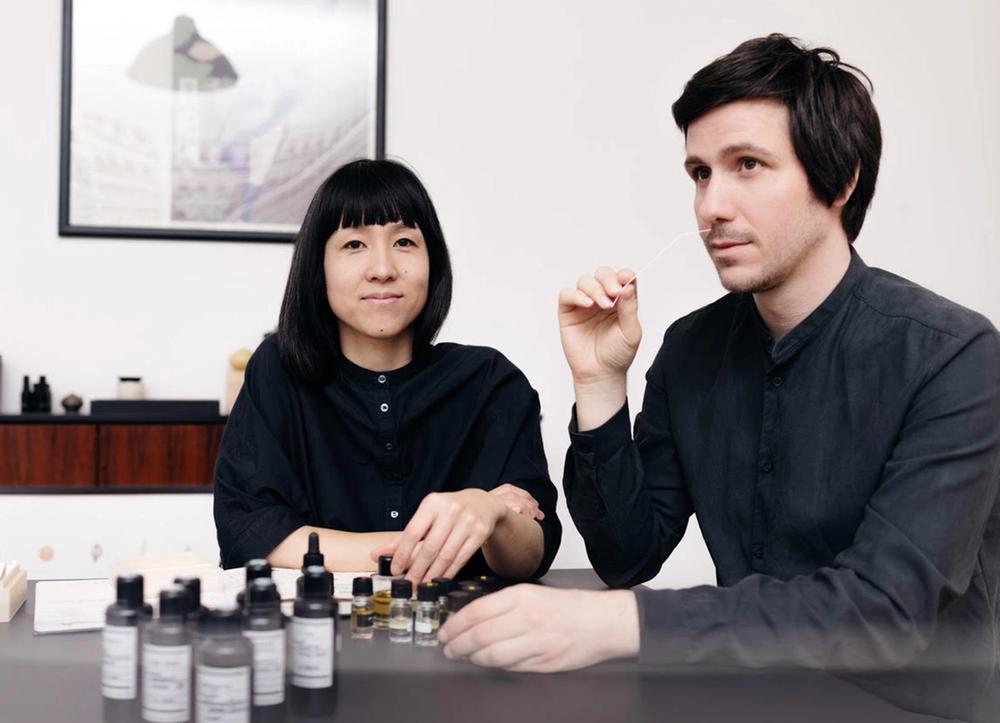A woman and a man smelling bottles of fragrances. 