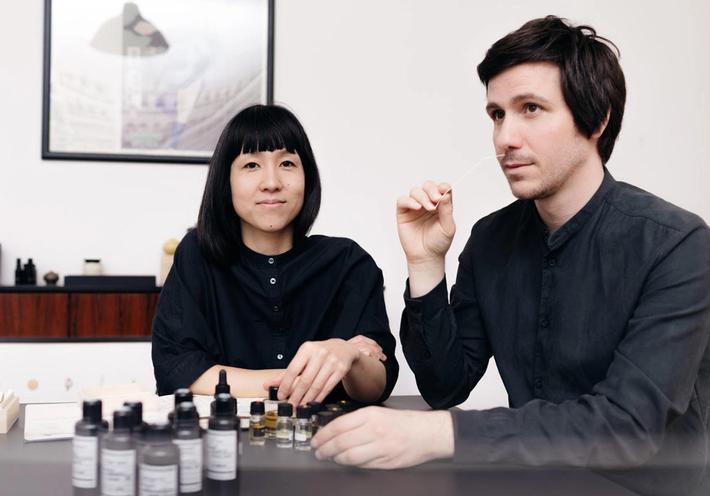 A woman and a man smelling bottles of fragrances. 