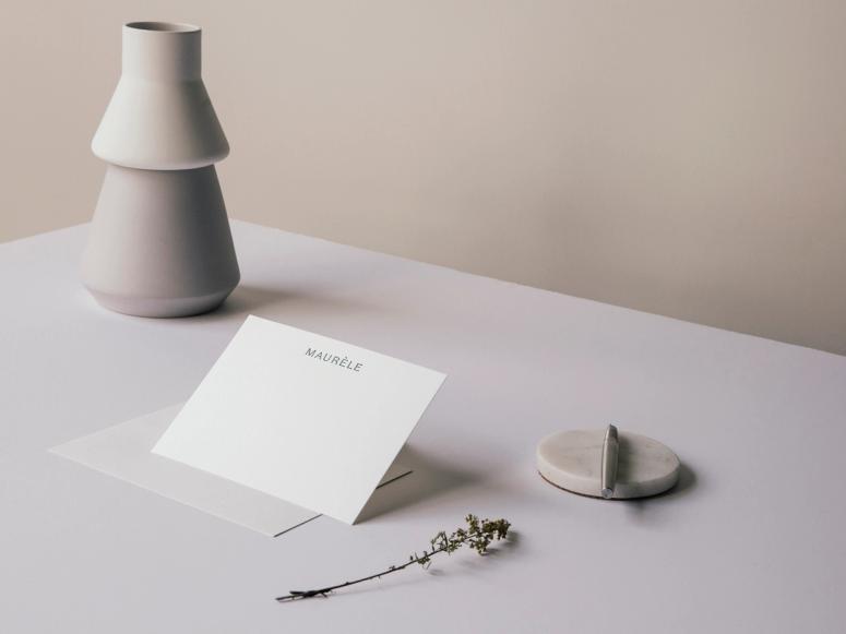 A note card on a desk with a pen, carafe, and sprig of herbs.