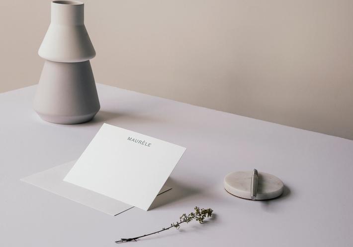A note card on a desk with a pen, carafe, and sprig of herbs.
