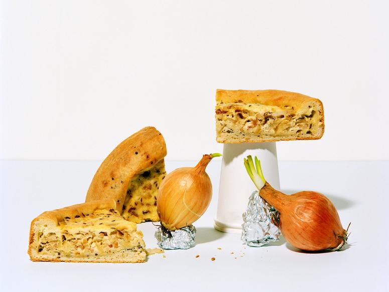 Slices of quiche arranged artfully with two onions, a takeout cup, and two pieces of tin foil.