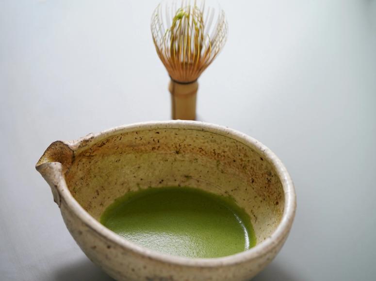 Matcha tea in a chawan in front of a matcha whisk.