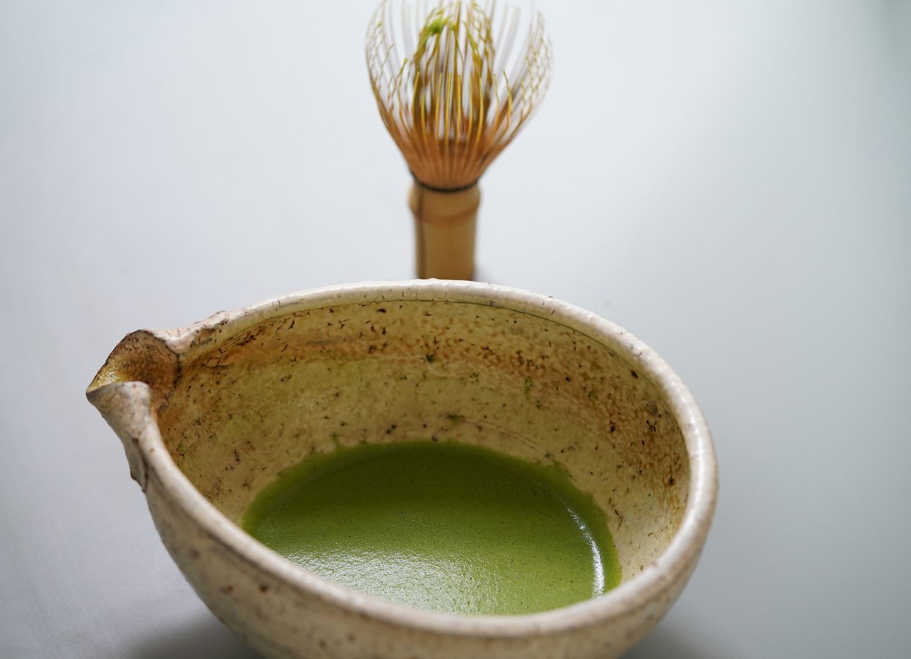 Matcha tea in a chawan in front of a matcha whisk.