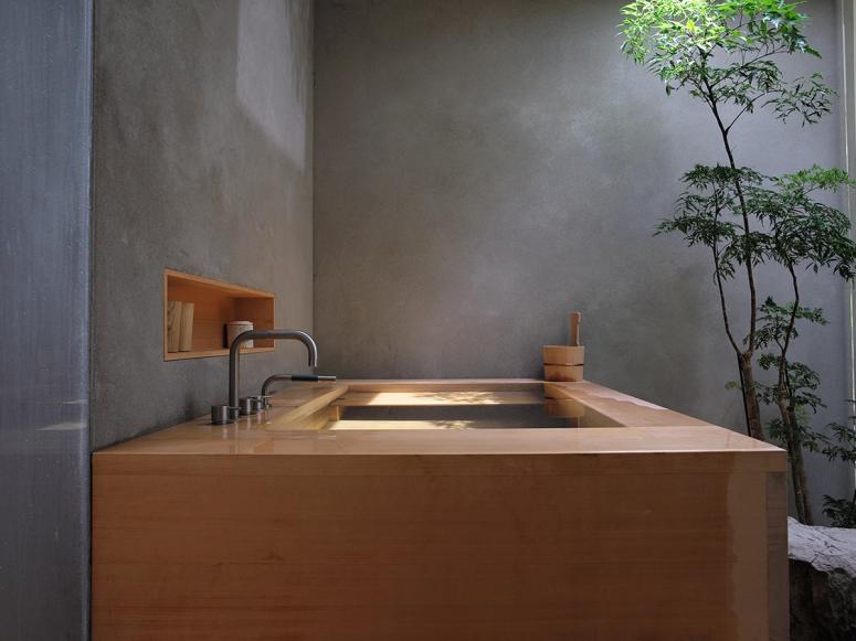 A hinoki bathtub in a concrete room with a small tree.