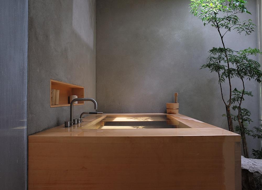 A hinoki bathtub in a concrete room with a small tree.