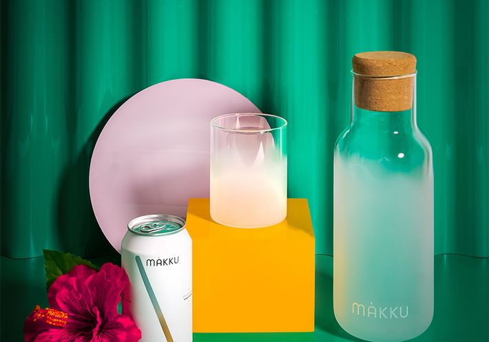 A carafe, glass, and can of Makku on a green backdrop.